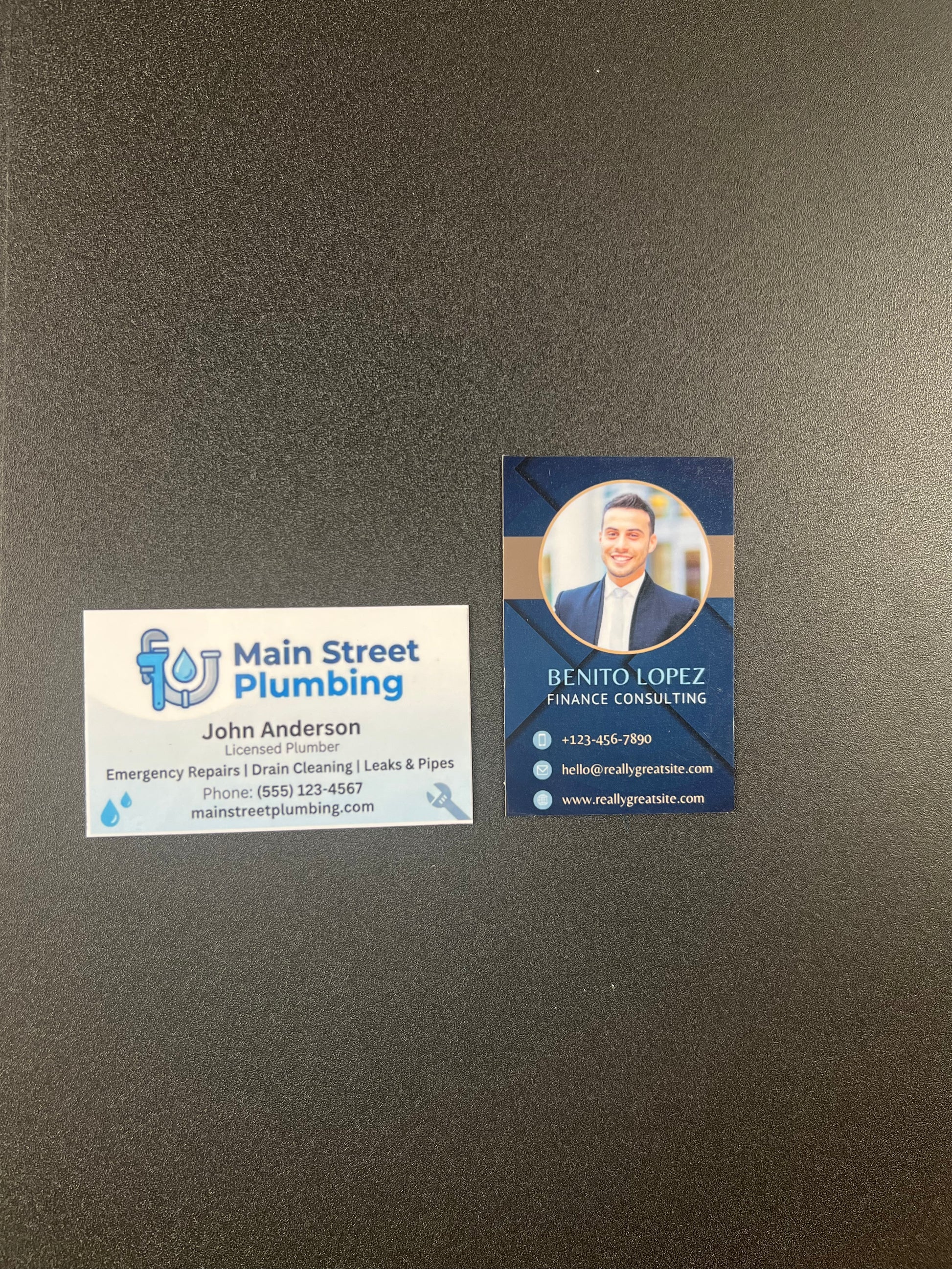 Two business cards on a dark surface, one for Main Street Plumbing and the other for Finance Consulting.