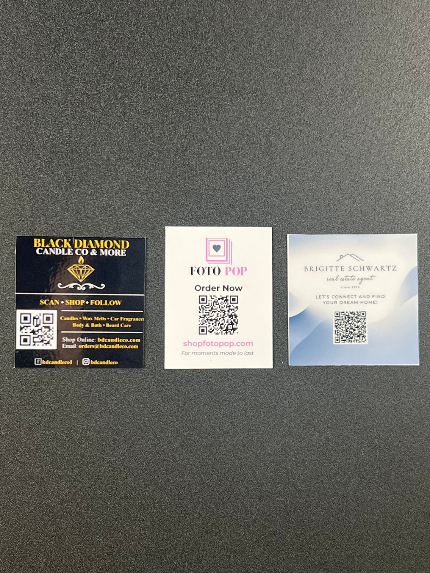 Three business cards on a gray surface with QR codes and contact information.